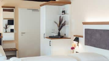 Ein Hotelzimmer mit einem Bett, einem Kleiderschrank, einer Ablage mit Flaschen und Gläsern sowie einem Nachttisch mit Lampe und Blumen.