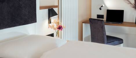 Una habitación de hotel moderna con una cama, un escritorio con una computadora portátil, un televisor y un florero con flores.
