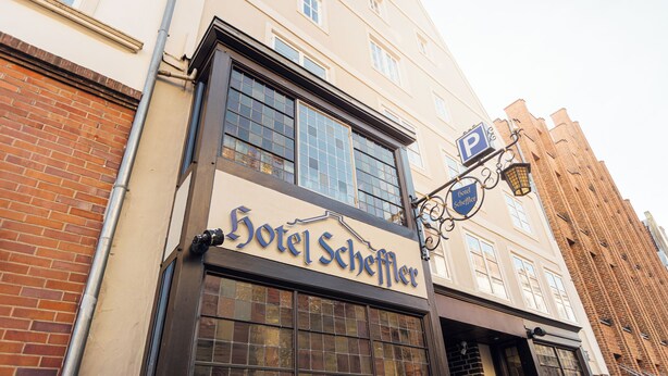 L’extérieur de l’hôtel Scheffler se distingue par une enseigne bien visible, de grandes fenêtres et une façade en briques.