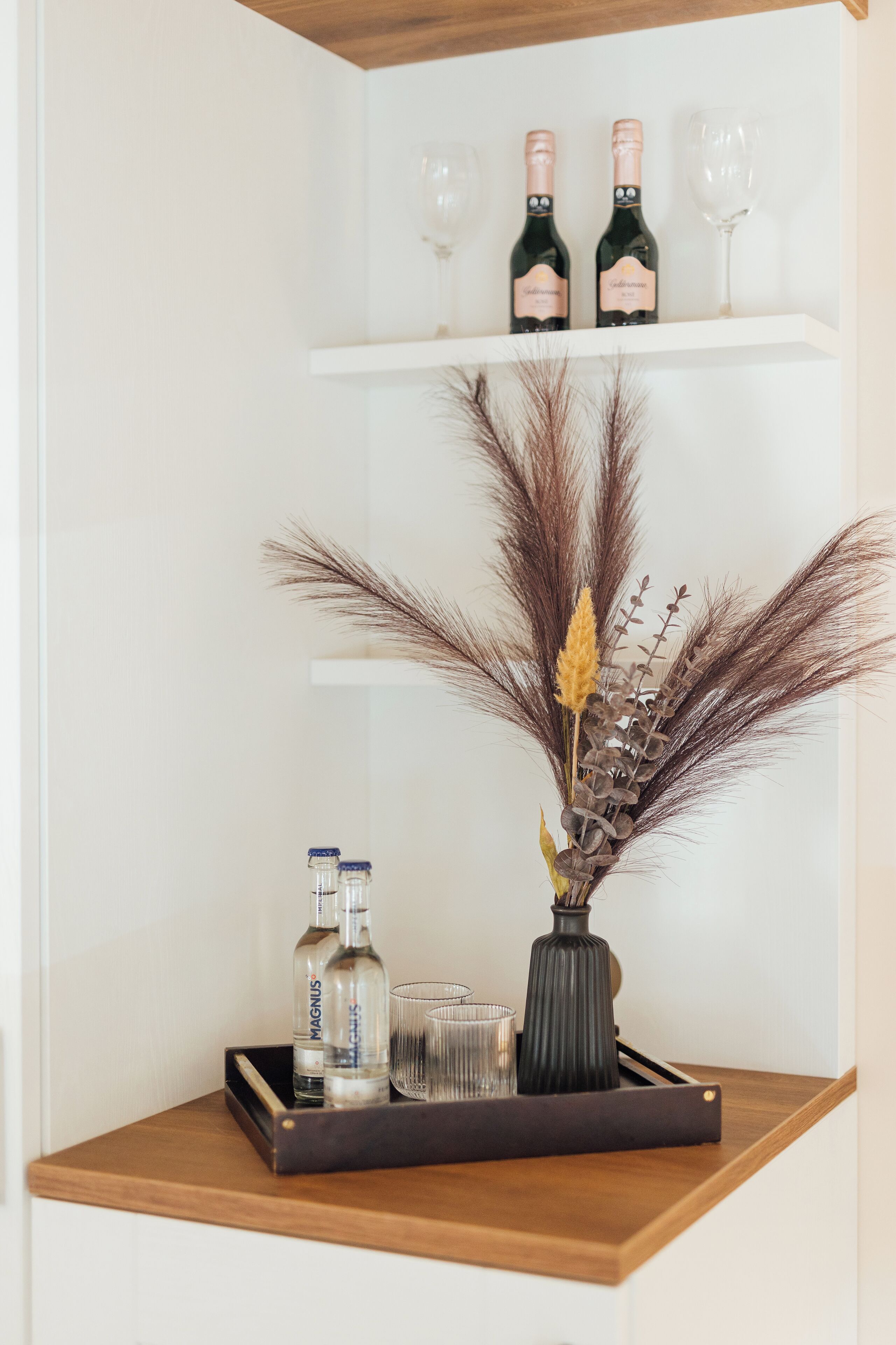 Ein Holzregal mit zwei Flaschen, einem Glas und dekorativen Pflanzen.