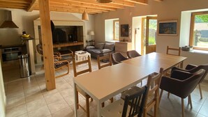 A spacious kitchen with wooden beams, a dining area with a long table and chairs, and a cozy living room with a sofa and fireplace. - Former Farm in the Loire Gorges—classified as a 3-star vacation rental (Vorey)