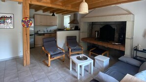 A spacious living area with a high wooden ceiling, a fireplace, a kitchen in the background, and two armchairs with a small table. - Former Farm in the Loire Gorges—classified as a 3-star vacation rental (Vorey)