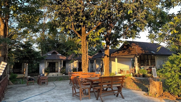 A courtyard with wooden benches and tables, surrounded by trees and buildings with tiled roofs. - A-Thip House (Pai)