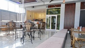 A spacious indoor area with a long bench, a dining table with chairs, and a kitchen in the background. - Hotel Drip Inn by RK (Rishikesh)