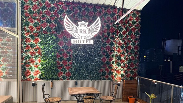 A balcony with a decorative wall featuring a logo and the text "RK HOTEL". There is a wooden table with chairs and a potted plant. - Hotel Drip Inn by RK (Rishikesh)
