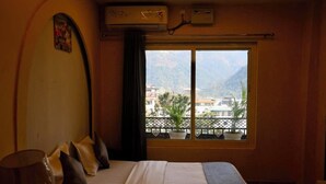 A hotel room with a bed, a window with a view of mountains, and an air conditioning unit. - Hotel Drip Inn by RK (Rishikesh)