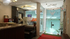 A hotel reception area with a marble counter, a sofa, a television, and a glass door leading to a pool area. - Hotel Drip Inn by RK (Rishikesh)