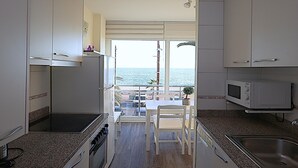 Kompakti keittiö, josta on näkymä merelle, ruokailutila pöydän ja tuolien kera sekä mikroaaltouuni.
