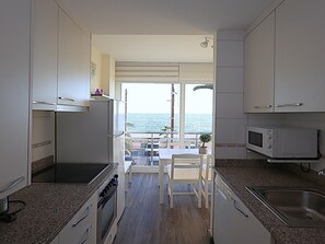 A compact kitchen with a view of the sea, a dining area with a table and chairs, and a microwave. - Diamonds Sea View – Apartamento frente al mar con terraza y capacidad para 6 personas (Lloret de Mar)
