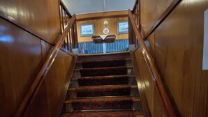 Un escalier en bois avec une rampe, des marches recouvertes de moquette et un luminaire au plafond.