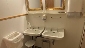 A bathroom with two sinks, a toilet, a small stool, and a mirror with an ornate frame.