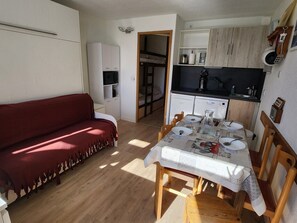 Un espace de vie compact comprenant un canapé rouge, une table à manger pour quatre personnes, un coin cuisine et une petite cuisine.