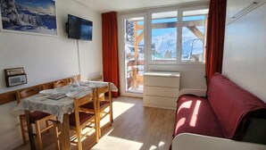 A cozy room with a dining table, chairs, a sofa, a TV, and a window with a view of snow-capped mountains. - Avoriaz - 4-person Apartment with TV and WiFi (Avoriaz)