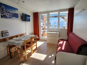 Une pièce chaleureuse comprenant une table à manger, des chaises, un canapé, un téléviseur et une fenêtre donnant sur des montagnes enneigées.