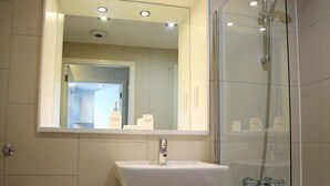 Baño con inodoro, lavamanos y ducha con mampara de vidrio.