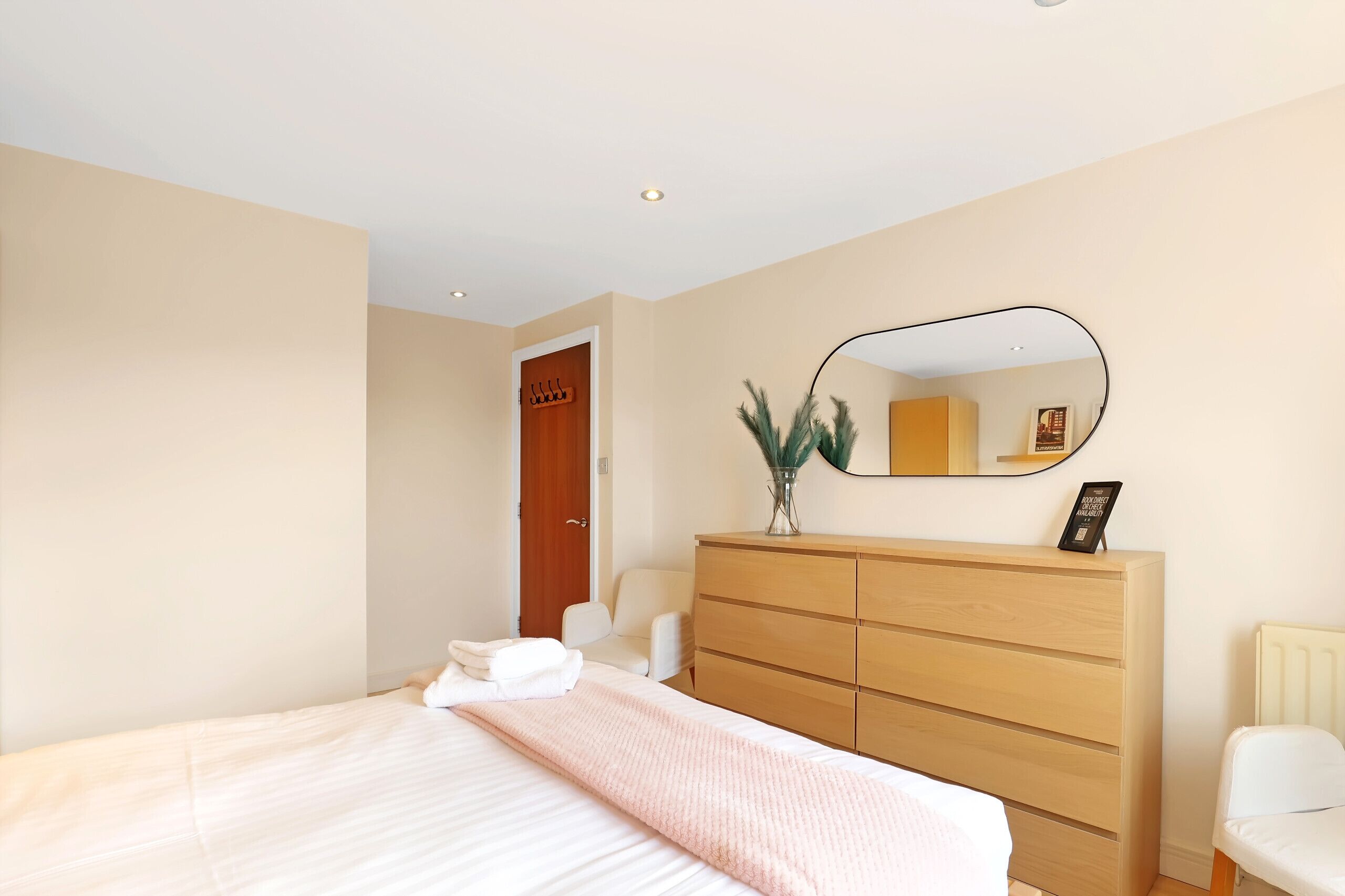 A bedroom with a bed, a wooden dresser, a mirror, and a chair.