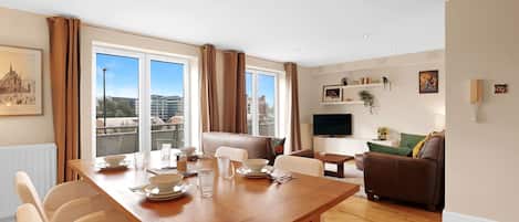 Una sala de estar moderna con comedor, ventanas amplias, un sofá y una televisión.