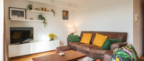 A living room with a brown leather sofa, a wooden coffee table, a flat-screen TV, and a white entertainment unit with shelves.