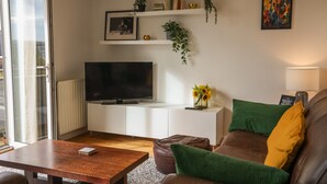 A modern living room with a flat-screen TV, a wooden coffee table, a brown leather sofa, a white console table with a vase of sunflowers, and a green and yellow pillow. - River View in Newcastle Upon Tyne (Newcastle-upon-Tyne)