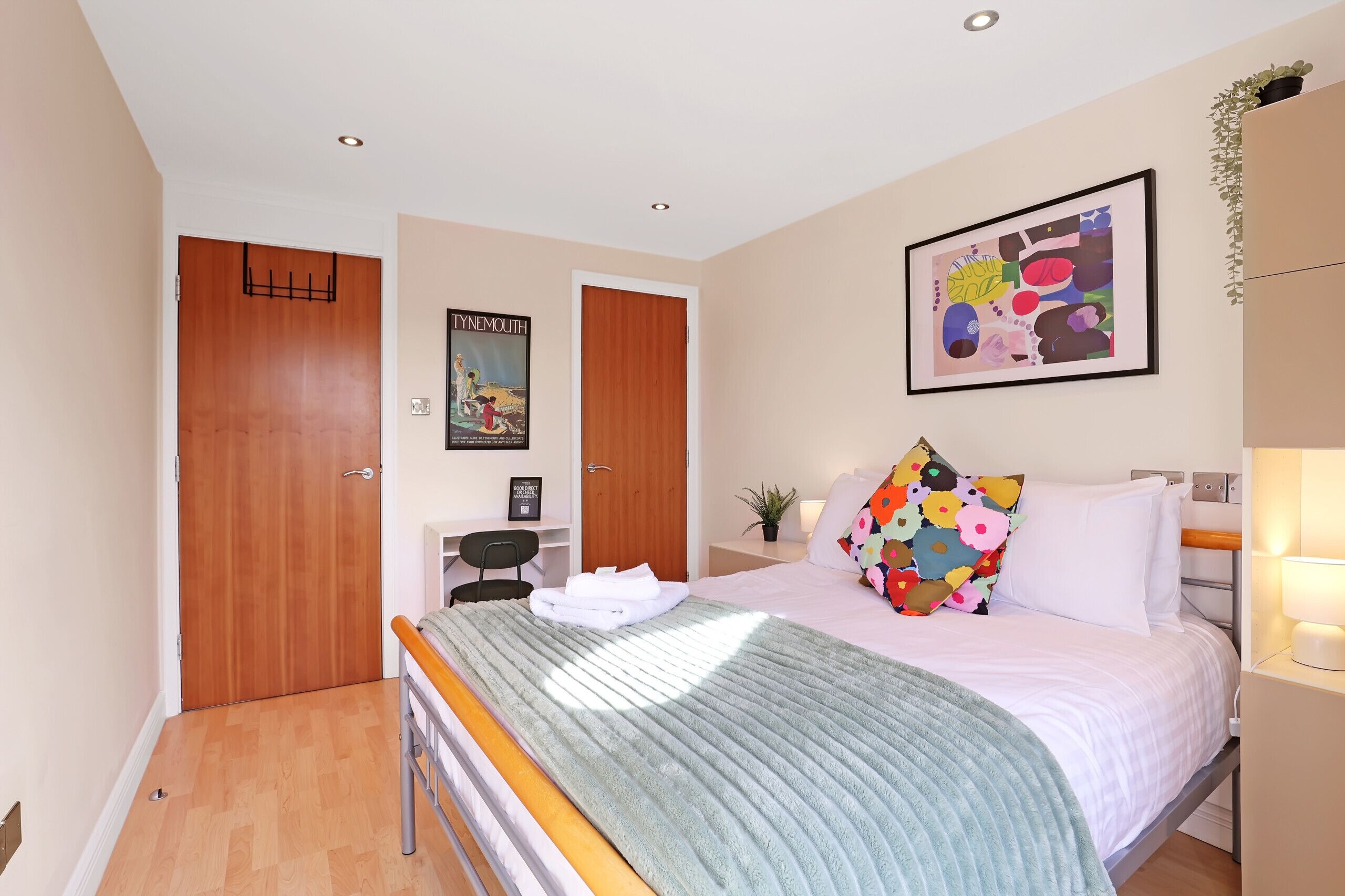 A bedroom with a bed, a desk, a chair, a wardrobe, and a poster on the wall.