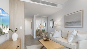 Ein modernes Wohnzimmer mit einem Holztisch, einem weißen Sofa mit gestreiften Kissen und einem großen gerahmten Kunstwerk an der Wand.