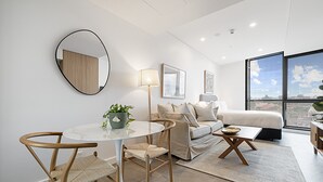 Ein modernes Wohnzimmer mit rundem Tisch, zwei Stühlen, einer Couch und einem großen Fenster mit Blick auf die Stadt.