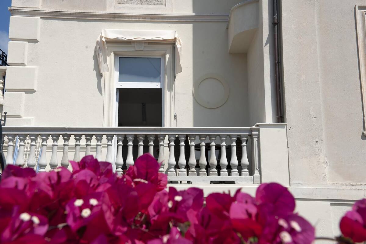 A building with a white facade, a balcony with balusters, and a window with a curtain.