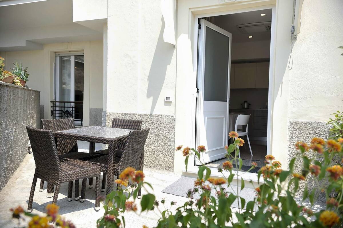 An outdoor patio with wicker furniture, a door leading to a kitchen, and potted plants.