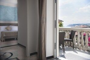 A hotel room with a bed, a view of the sea, and a balcony with wicker chairs. - Hotel Villa Centa (Varazze)