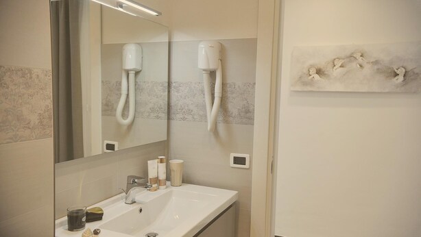 A bathroom with a sink, mirror, hairdryer, and a wall-mounted towel rack. - Hotel Villa Centa (Varazze)