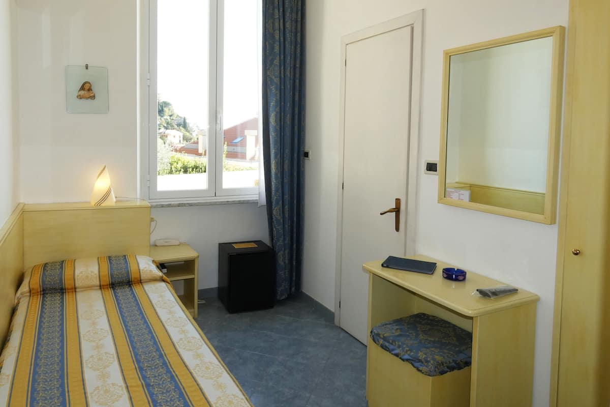 A hotel room with a bed, bedside table, lamp, dresser, mirror, and a window with curtains.