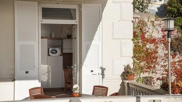 A balcony with a view of a garden, a door leading to a room with a microwave, and a chair.
