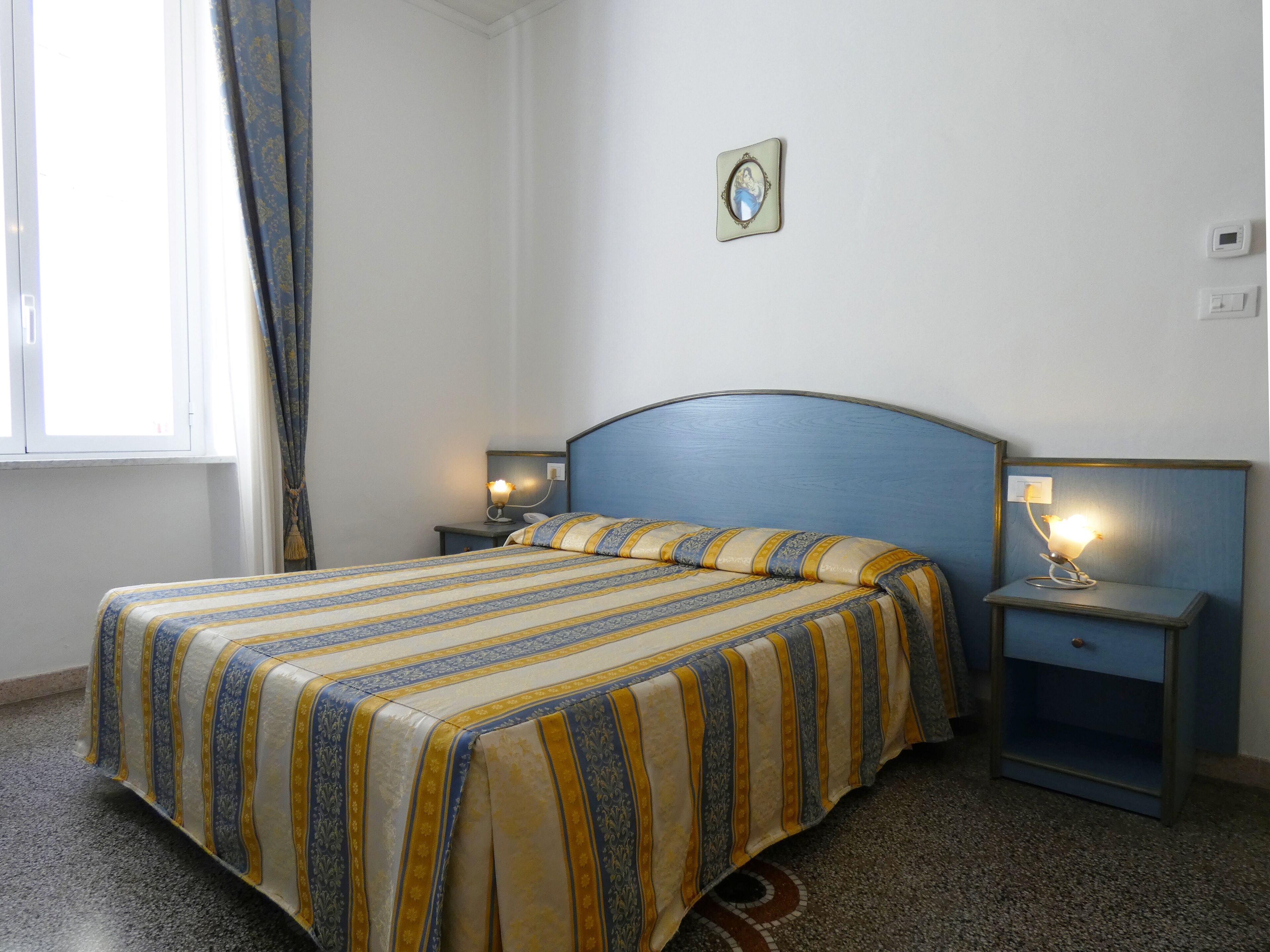 Un lit bien fait, avec une literie à rayures, deux tables de chevet avec des lampes, une fenêtre avec des rideaux et un tableau accroché au mur.