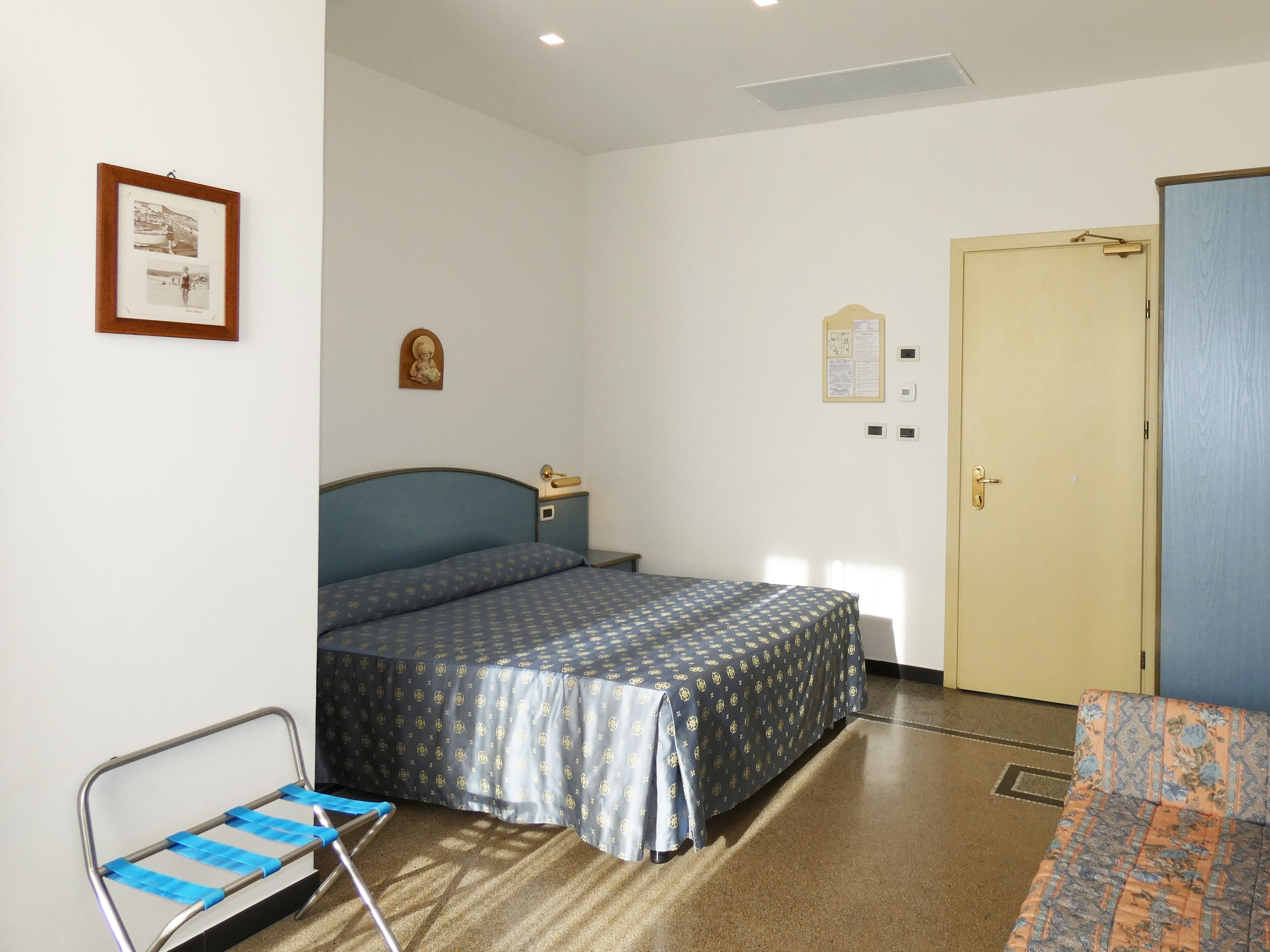 Un dormitorio con una cama, una silla, una puerta y un cuadro en la pared.