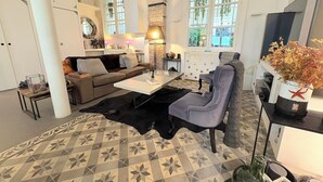 Una sala de estar moderna con un sofá, una mesa de centro y una silla. Hay una alfombra estampada en el suelo y una planta en maceta sobre una mesita auxiliar.
