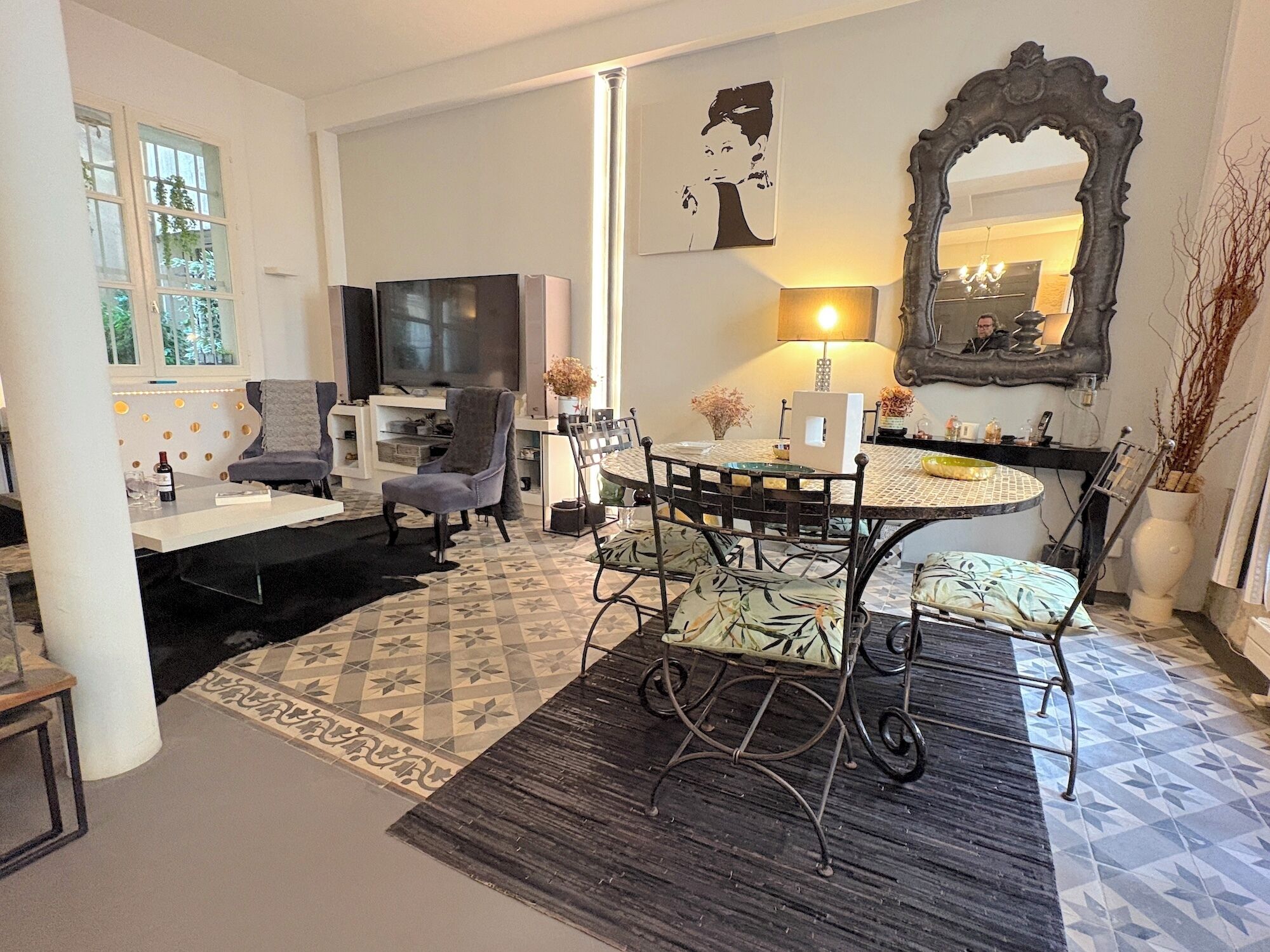 A living room with a TV, sofa, chairs, a dining table, and a patterned rug.