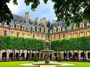 A courtyard with a fountain, surrounded by a building with multiple windows and a symmetrical facade. - Le Loft Villehardouin (Paris 03)