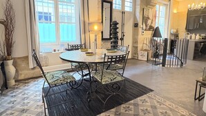 Un comedor con una mesa redonda, sillas y una alfombra negra. Hay una ventana con cortinas, una lámpara y un espejo en la pared.