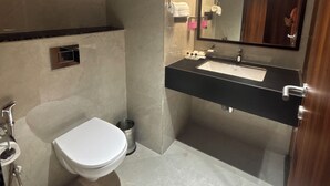 Un baño moderno con un inodoro blanco, un lavamanos negro y un espejo grande.