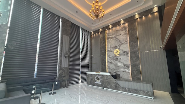 Un lobby moderno con una recepción de mármol, un candelabro y una zona de estar con sofás y mesas.