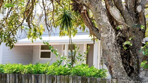 A house with a wooden fence, a large tree, and a small plant in the yard. - Seeside Cottage Bargara | Beach 100m | Pet-Friendly | Sleeps 6 (Bargara)