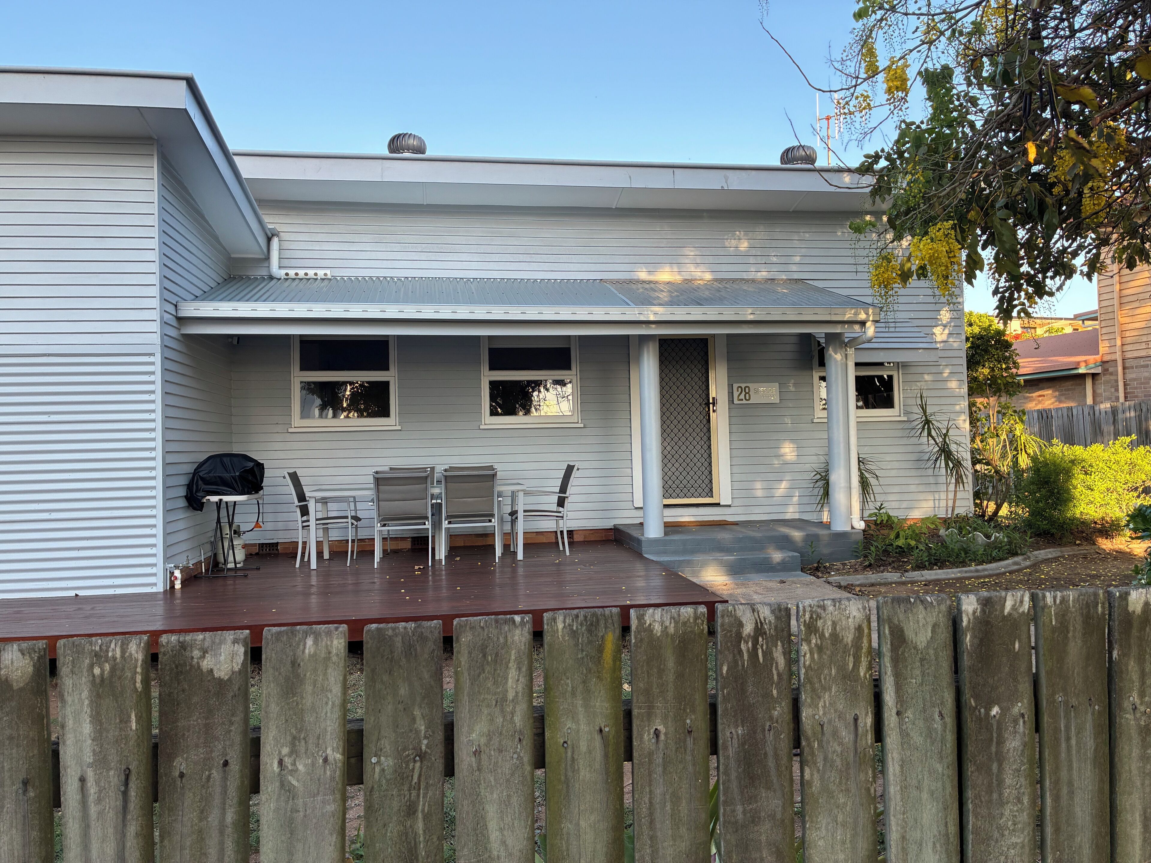 Une maison de plain-pied avec un patio couvert, une plaque portant le numéro 28 et une clôture en bois.