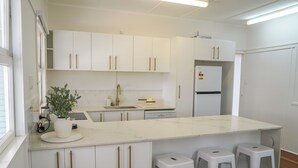 A modern kitchen with white cabinets, a marble countertop, a refrigerator, and a potted plant. - Seeside Cottage Bargara | Beach 100m | Pet-Friendly | Sleeps 6 (Bargara)