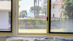 A bedroom with a bed, pillows, and a window overlooking a residential area with a fence, trees, and a parked car. - Seeside Cottage Bargara | Beach 100m | Pet-Friendly | Sleeps 6 (Bargara)