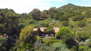 A hillside villa with a patio area, surrounded by dense greenery and a hilltop structure.