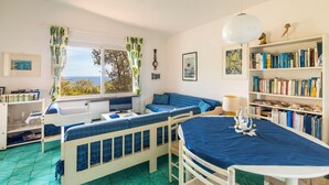 A cozy room with a bed, a desk, a bookshelf, and a view of the sea.