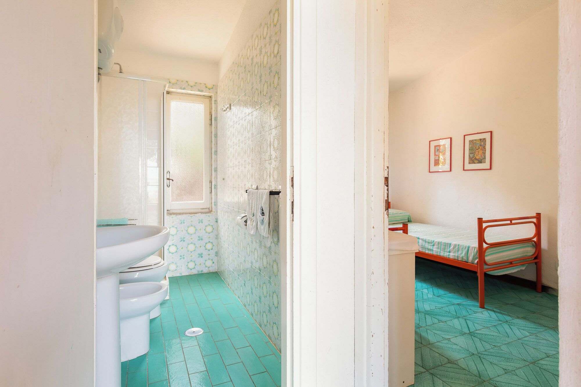 A narrow room with a toilet, sink, and a bed with a metal frame.