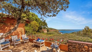 An outdoor seating area with stone walls, a table, and chairs overlooking a coastal view.