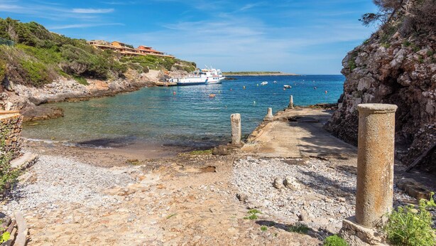 A coastal pathway leading to a rocky shore with a boat docked nearby.