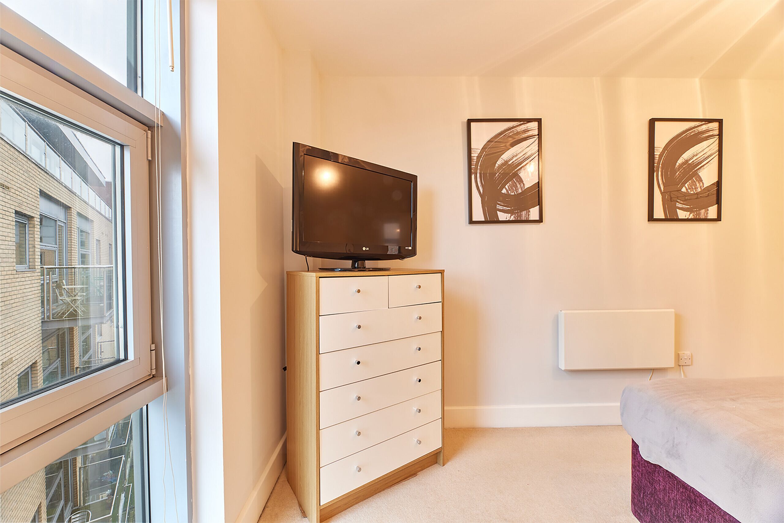 A bedroom with a bed, a dresser, a TV, and two abstract art pieces on the wall.